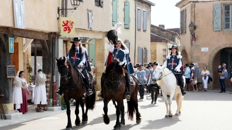 L'arrivée de d'Artagnan dans Lupiac sur son cheval, suivi des mousquetaires, avec des personnes en costume d'époque et des visiteurs